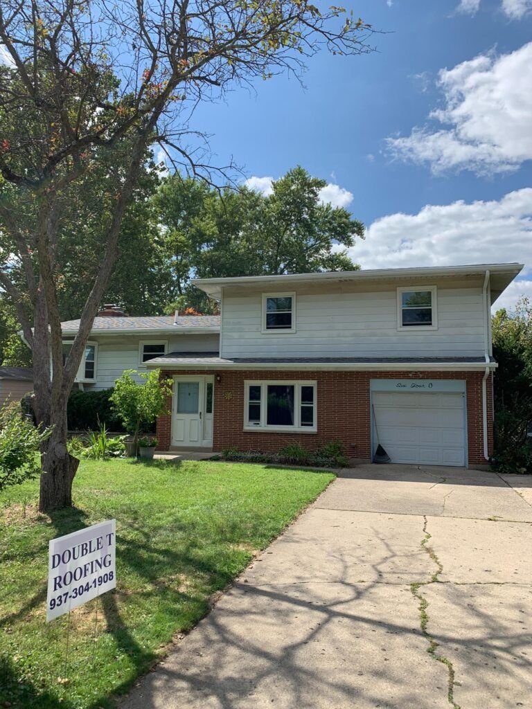 Two-story house with brick and white siding, garage, and a cracked driveway on a sunny day.