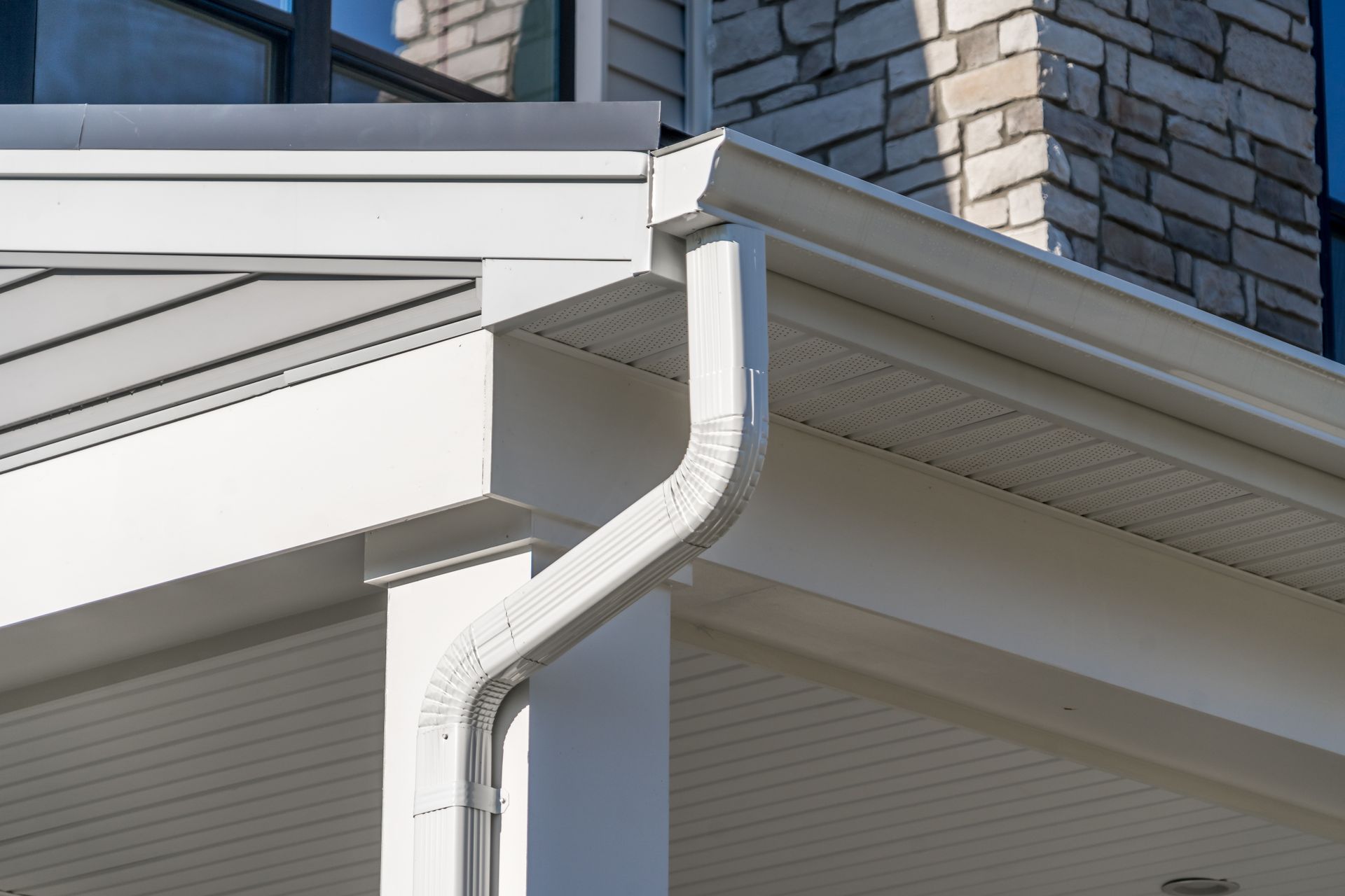 White rain gutter and downspout on a house with stone and white siding.