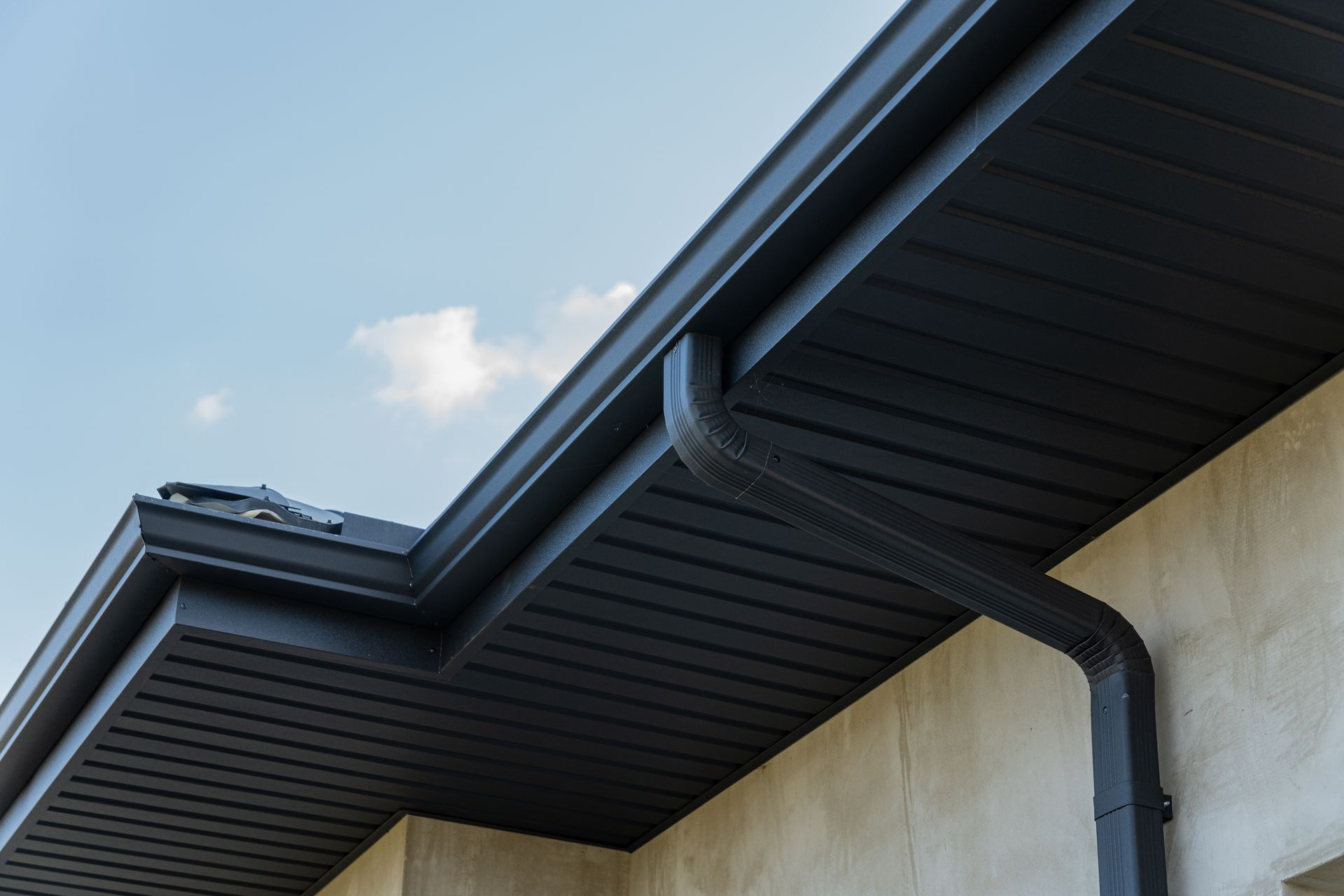 Black rain gutter and downspout on a building with a light blue sky.