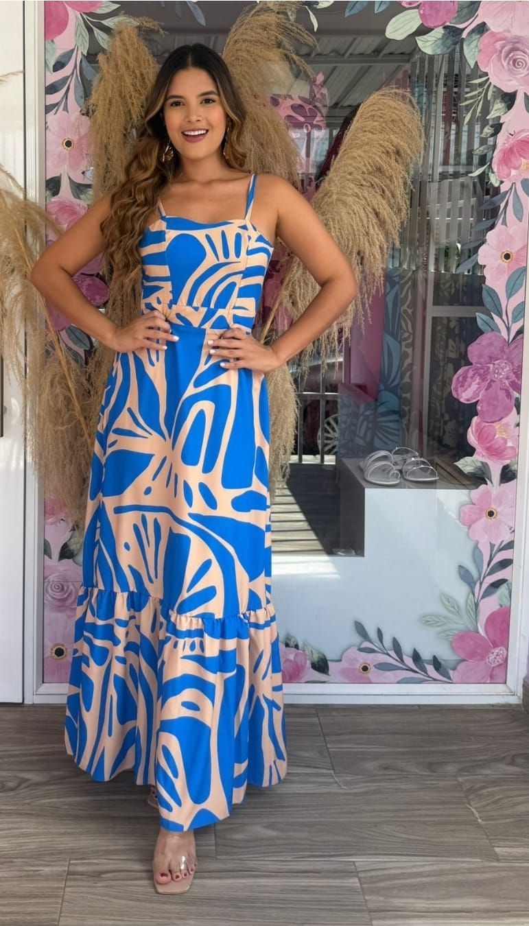 Una mujer con un vestido azul y blanco está parada frente a una pared floral.