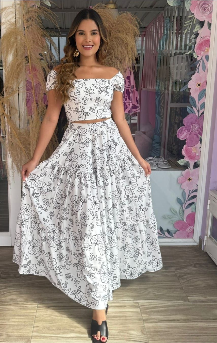 Una mujer lleva un top blanco y una falda blanca con flores.