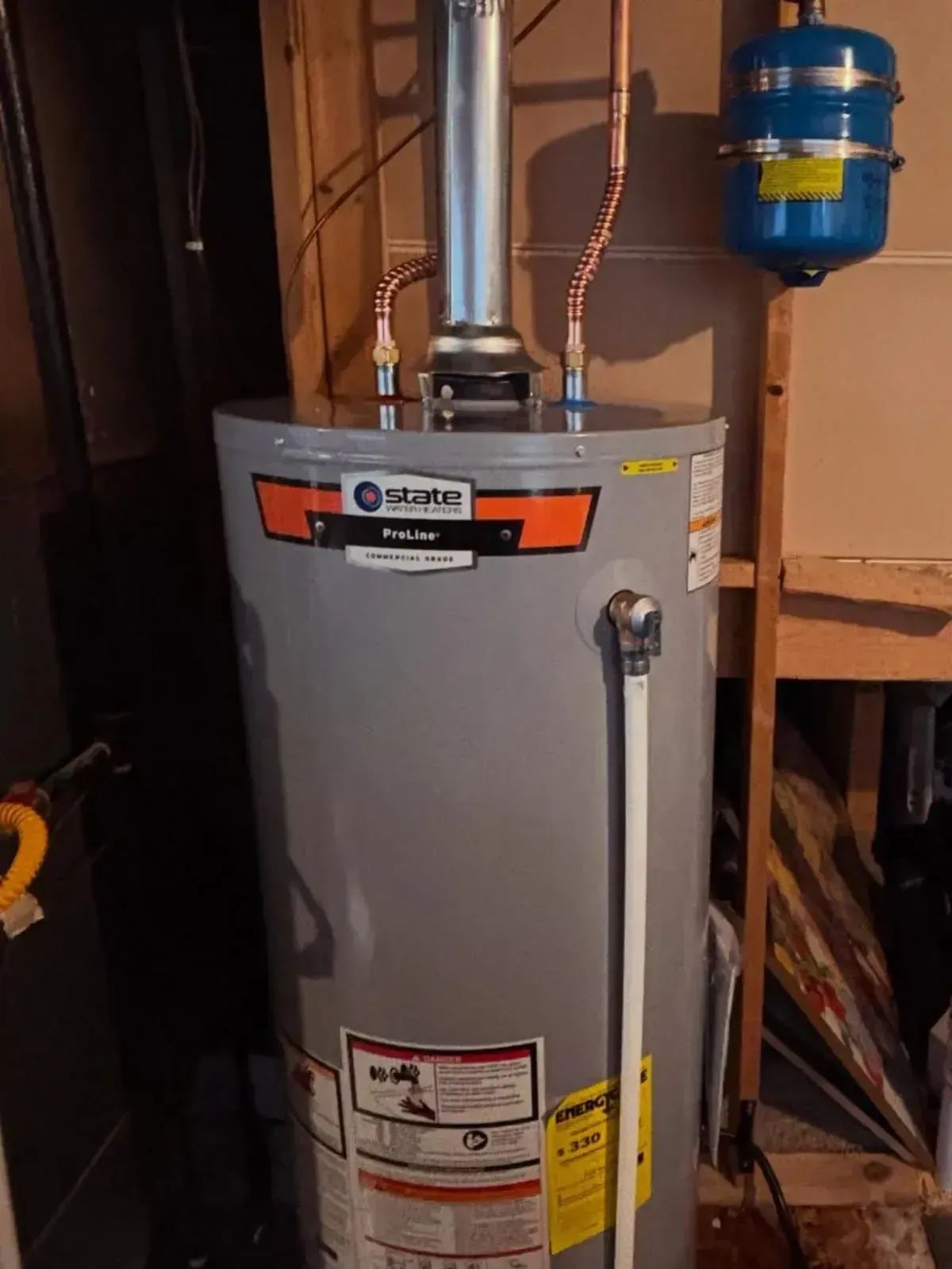 A gray State brand residential gas water heater with copper piping and an expansion tank in a basement setting.