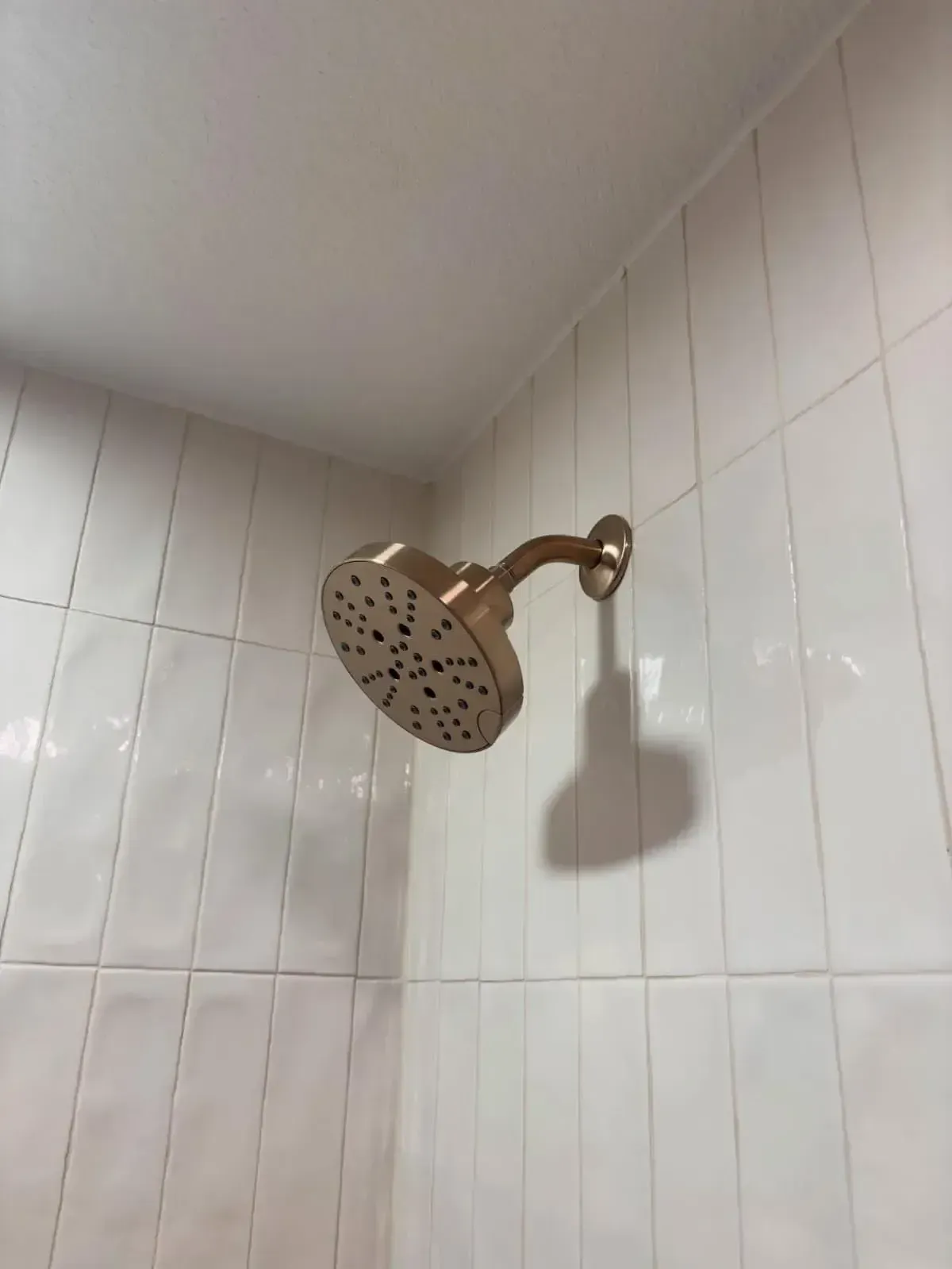 A gold shower head mounted on a white, vertical tiled shower wall.