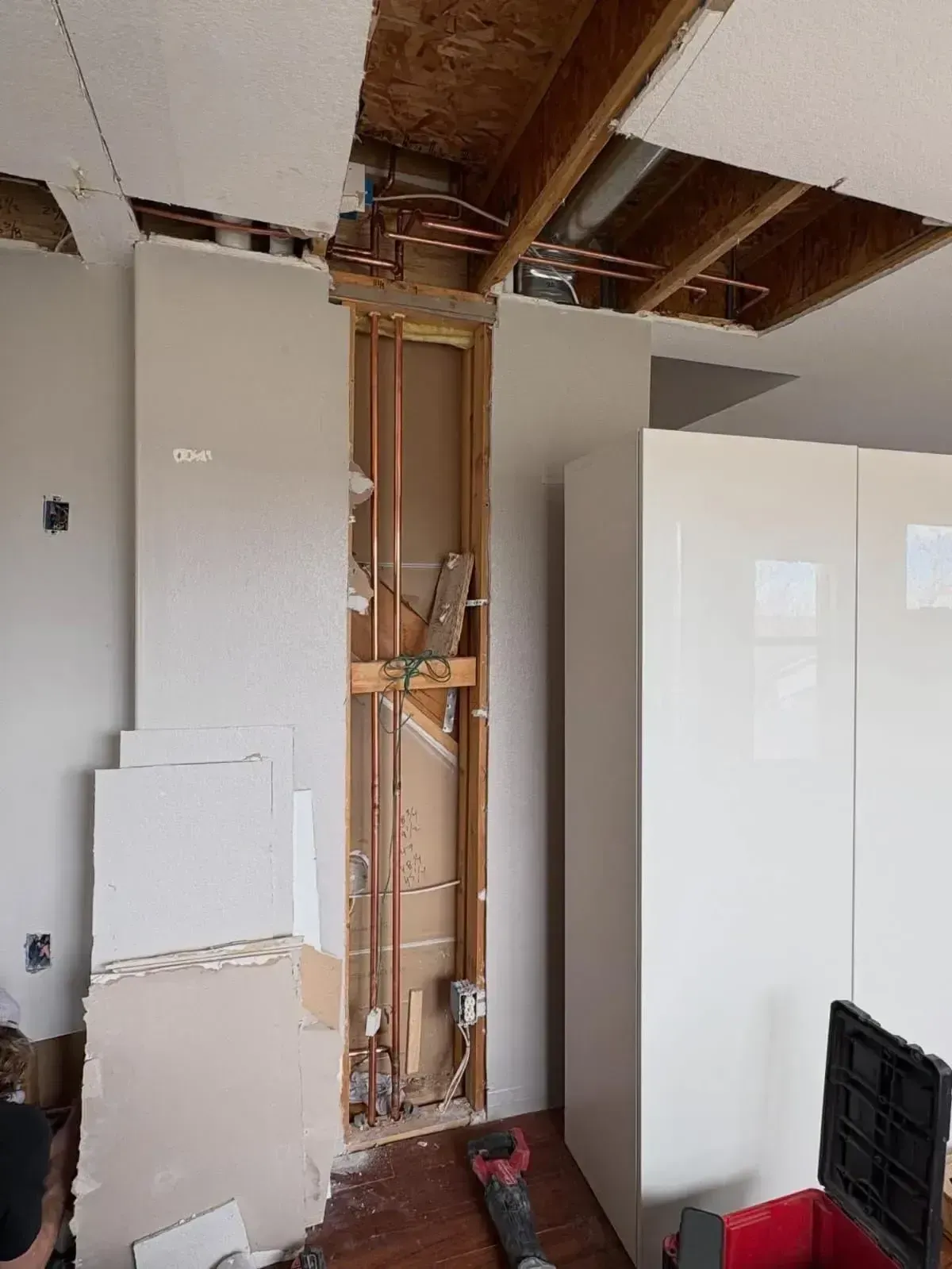 An unfinished interior wall with exposed copper pipes and wood framing, viewed beneath an open ceiling with ductwork.