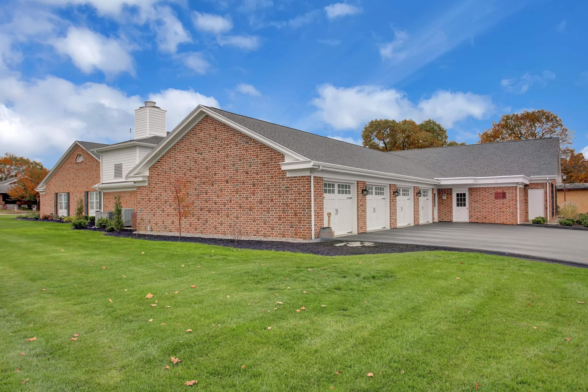 A large brick house with two garages and a large lawn in front of it.