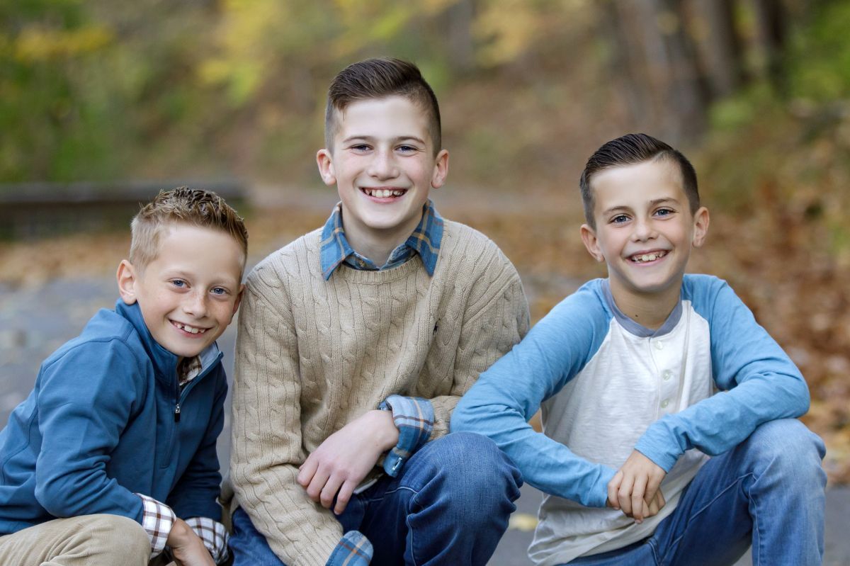 Three young boys are sitting next to each other on the ground and smiling for the camera.