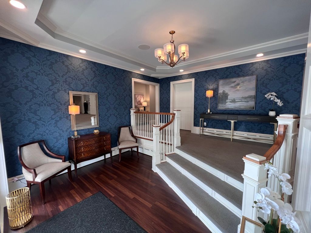A living room with blue walls , chairs , stairs and a chandelier.