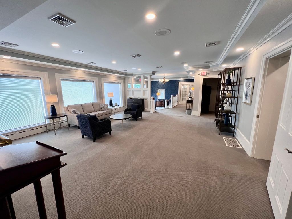 A large living room with a couch , chairs , tables and a piano.