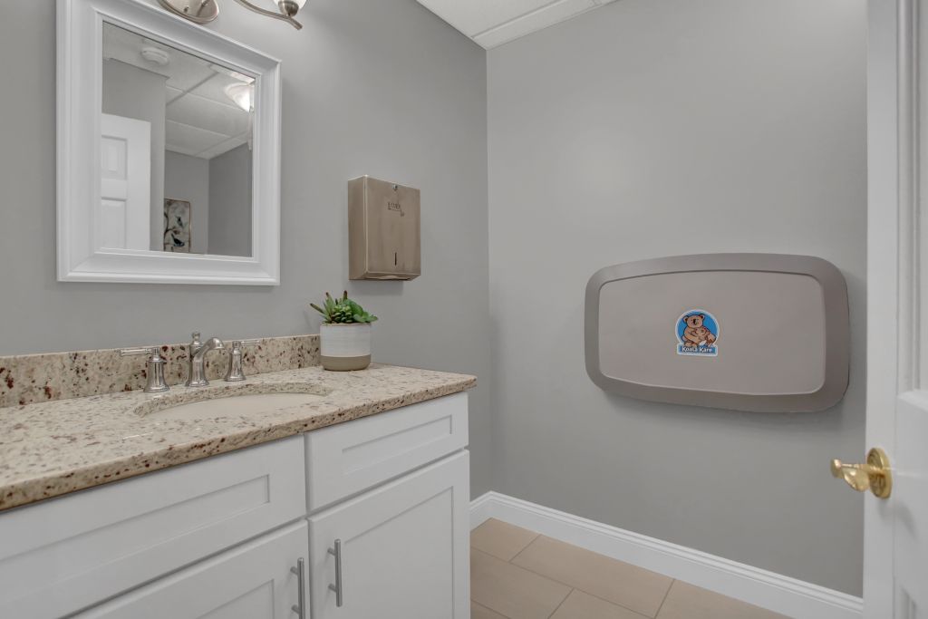 A bathroom with a sink , mirror and changing table.