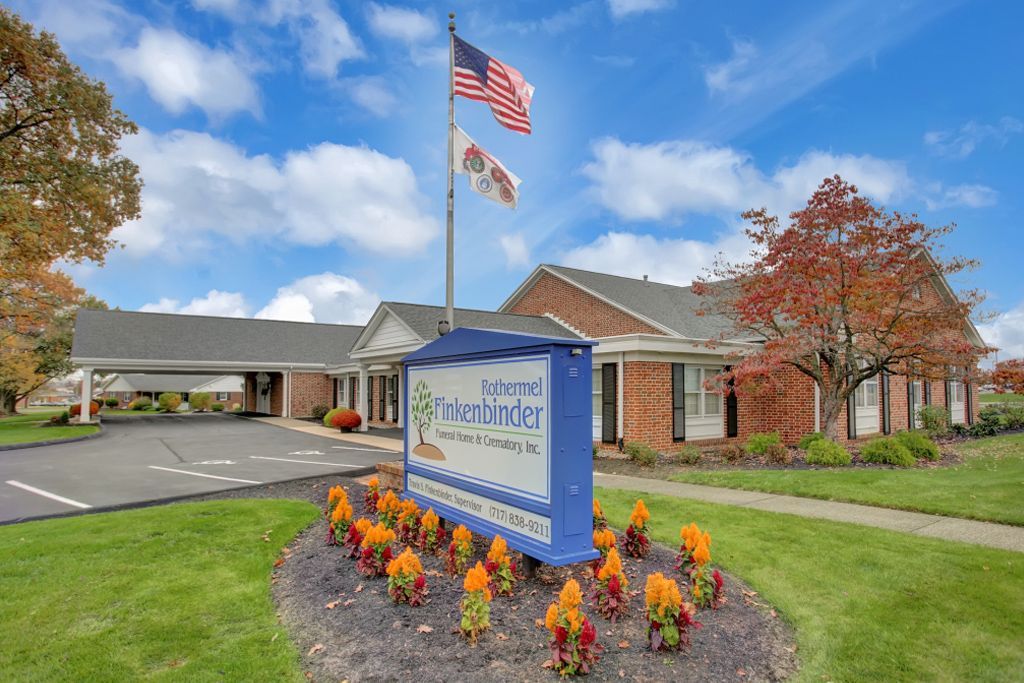 There is a sign in front of a building with flowers in front of it.