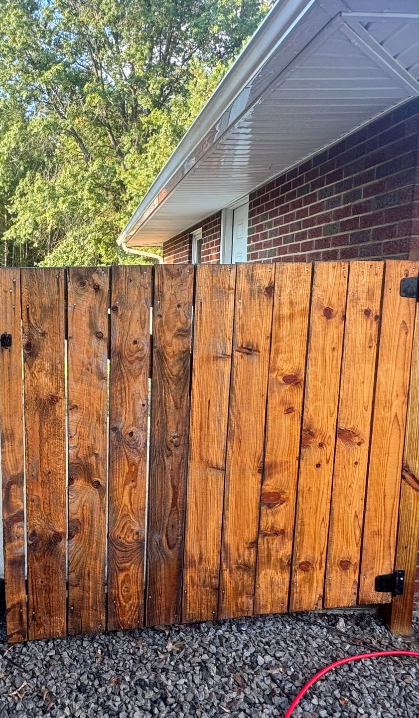 Wooden gate with warm brown stain next to a brick wall and white gutter.