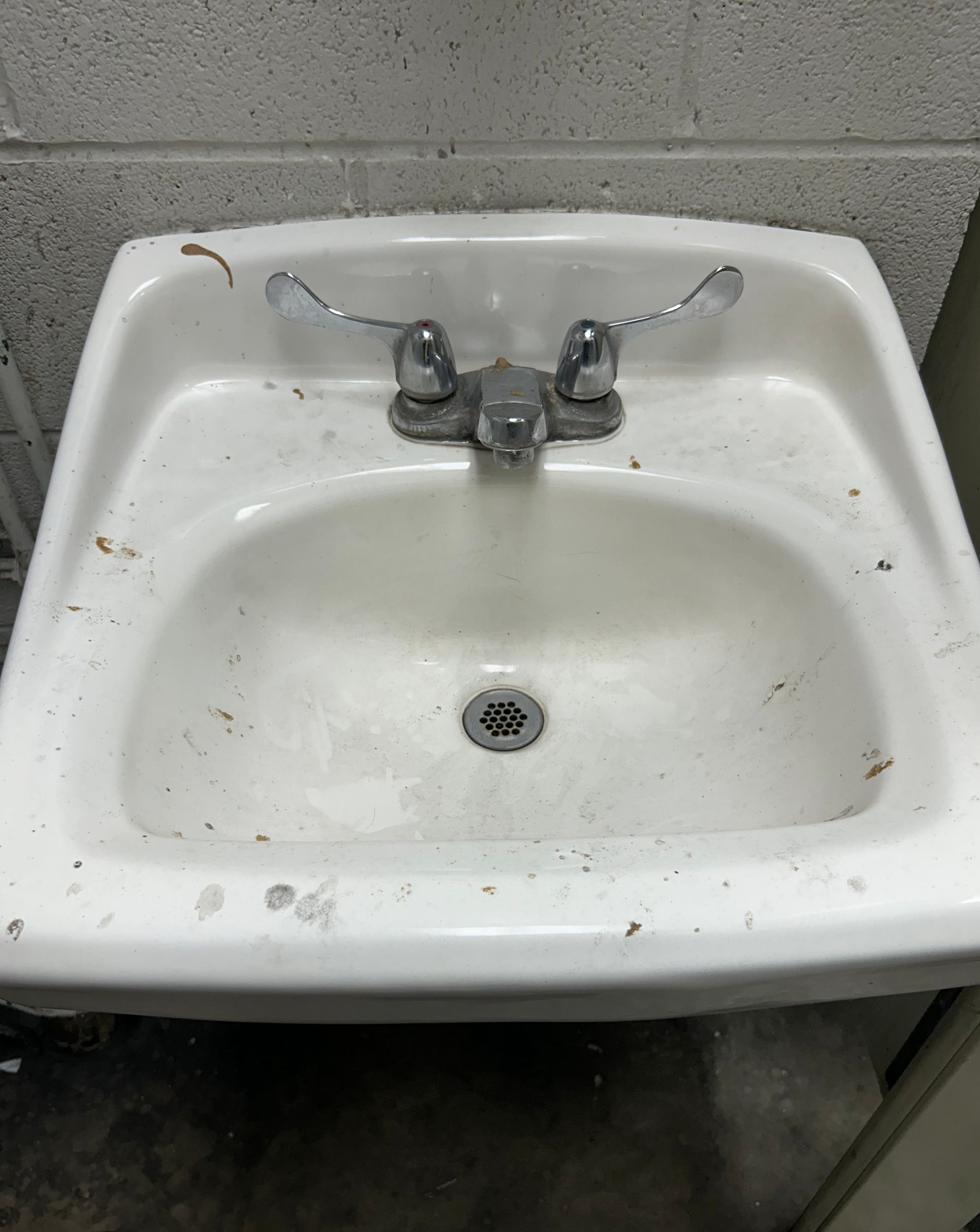 White, dirty utility sink with silver faucet and handles; located indoors.