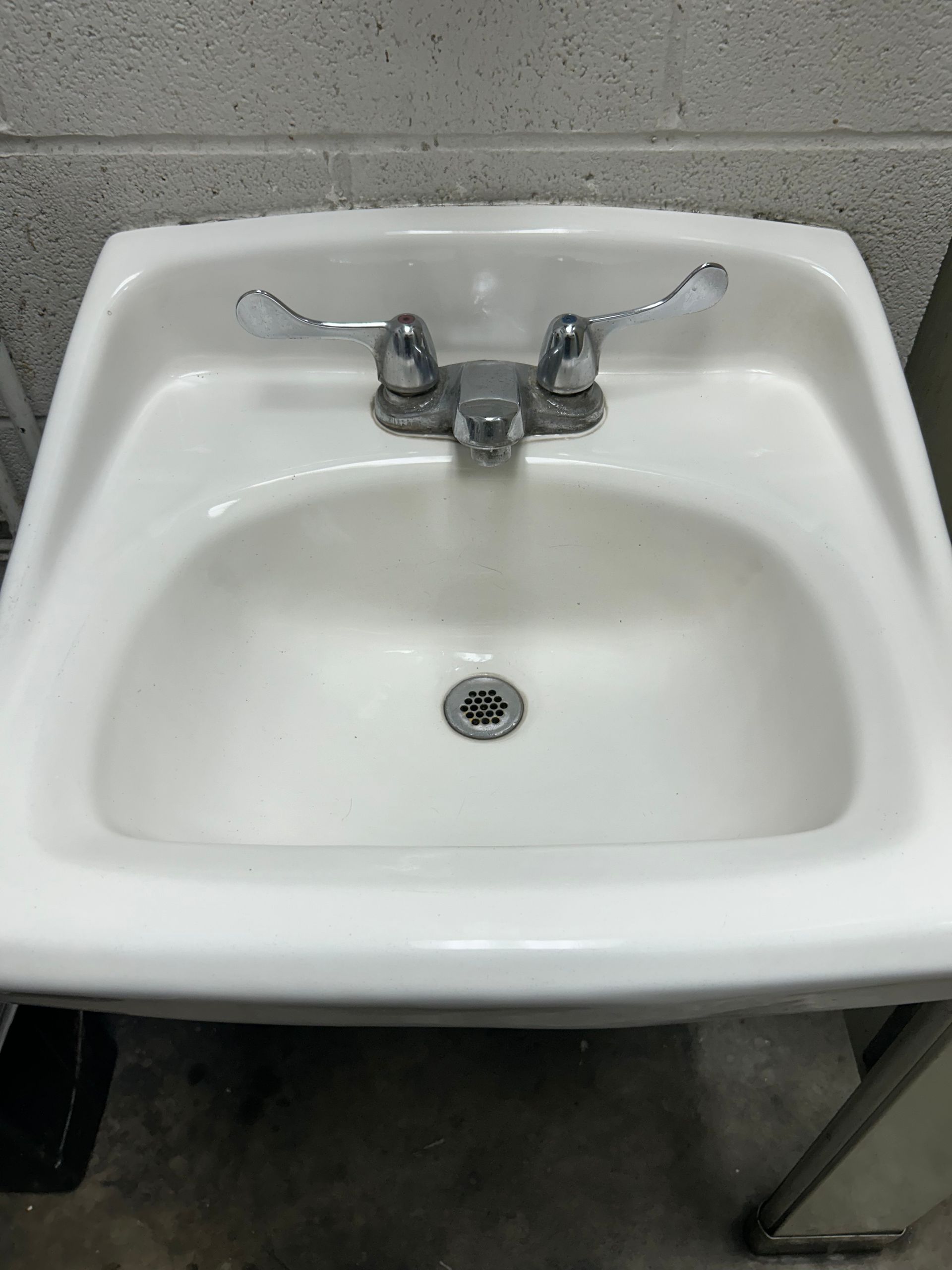 White ceramic sink with chrome faucet and handles in a utility setting.