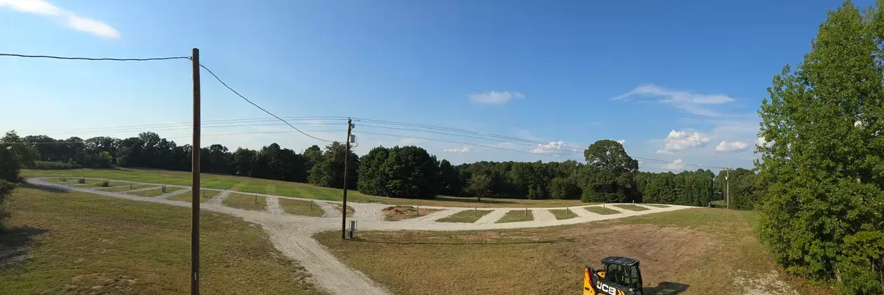 A sunny day with a cleared field with small gravel pads, trees, and a utility pole under a blue sky.