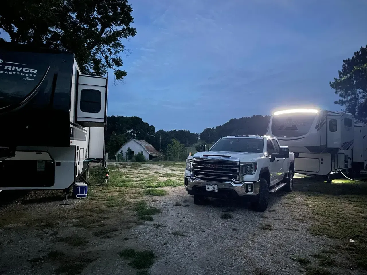 Truck parked between two RVs on a gravel lot at dusk. A distant, small building is visible.