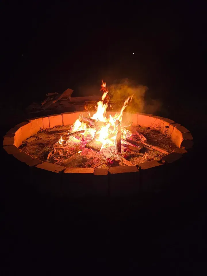 Campfire burning brightly in a circular brick fire pit at night.