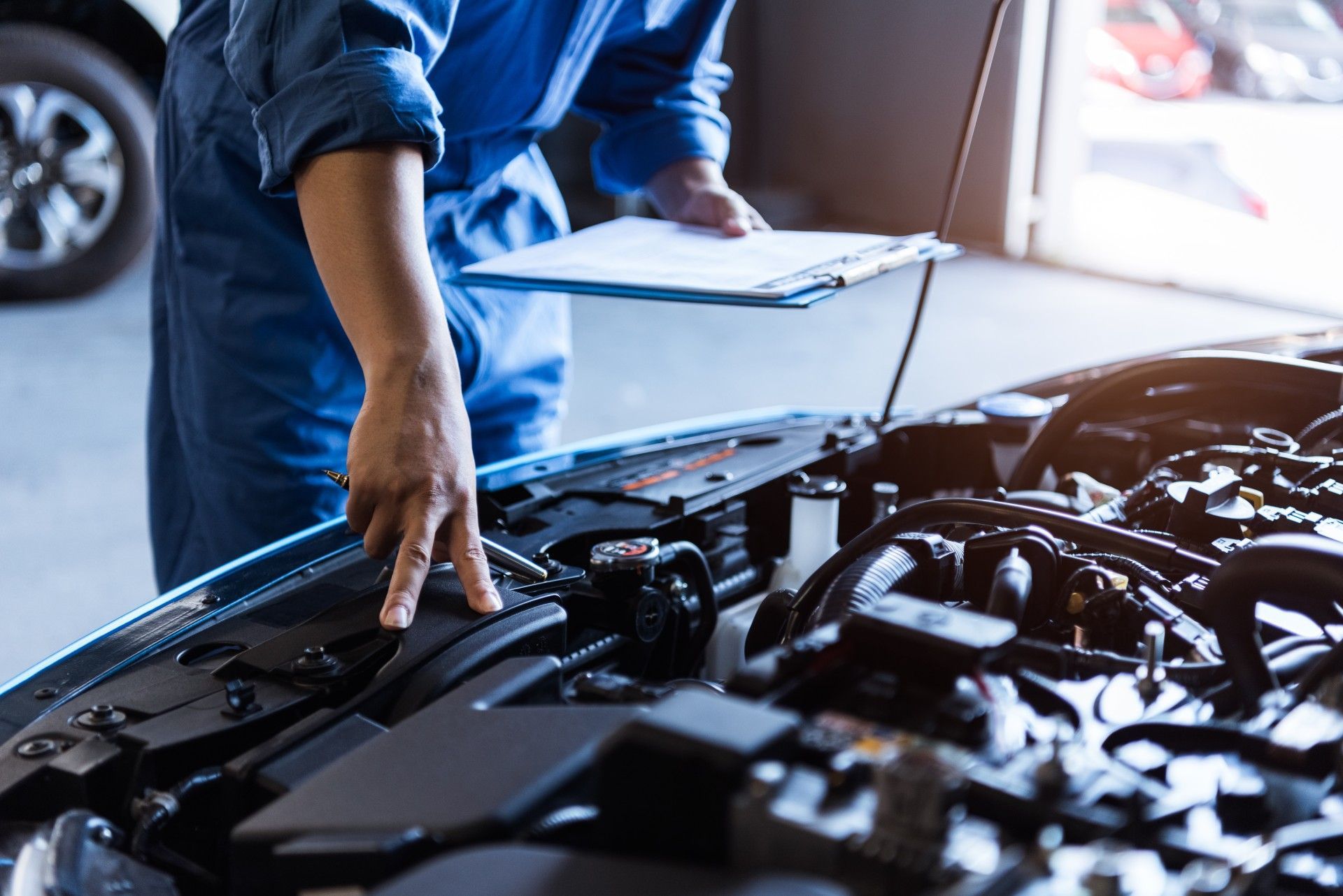 A mechanic is looking under the hood of a car while holding a clipboard.