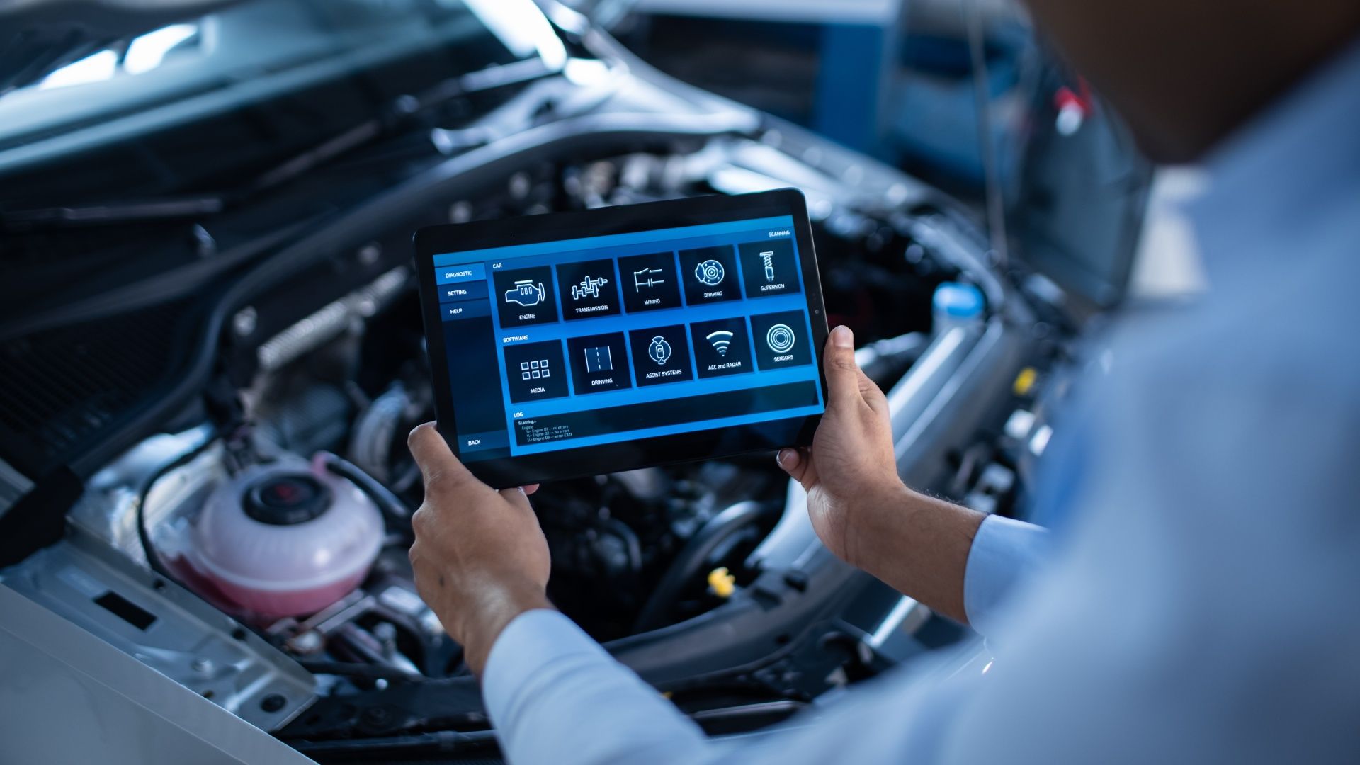 A mechanic is using a tablet to check the engine of a car.