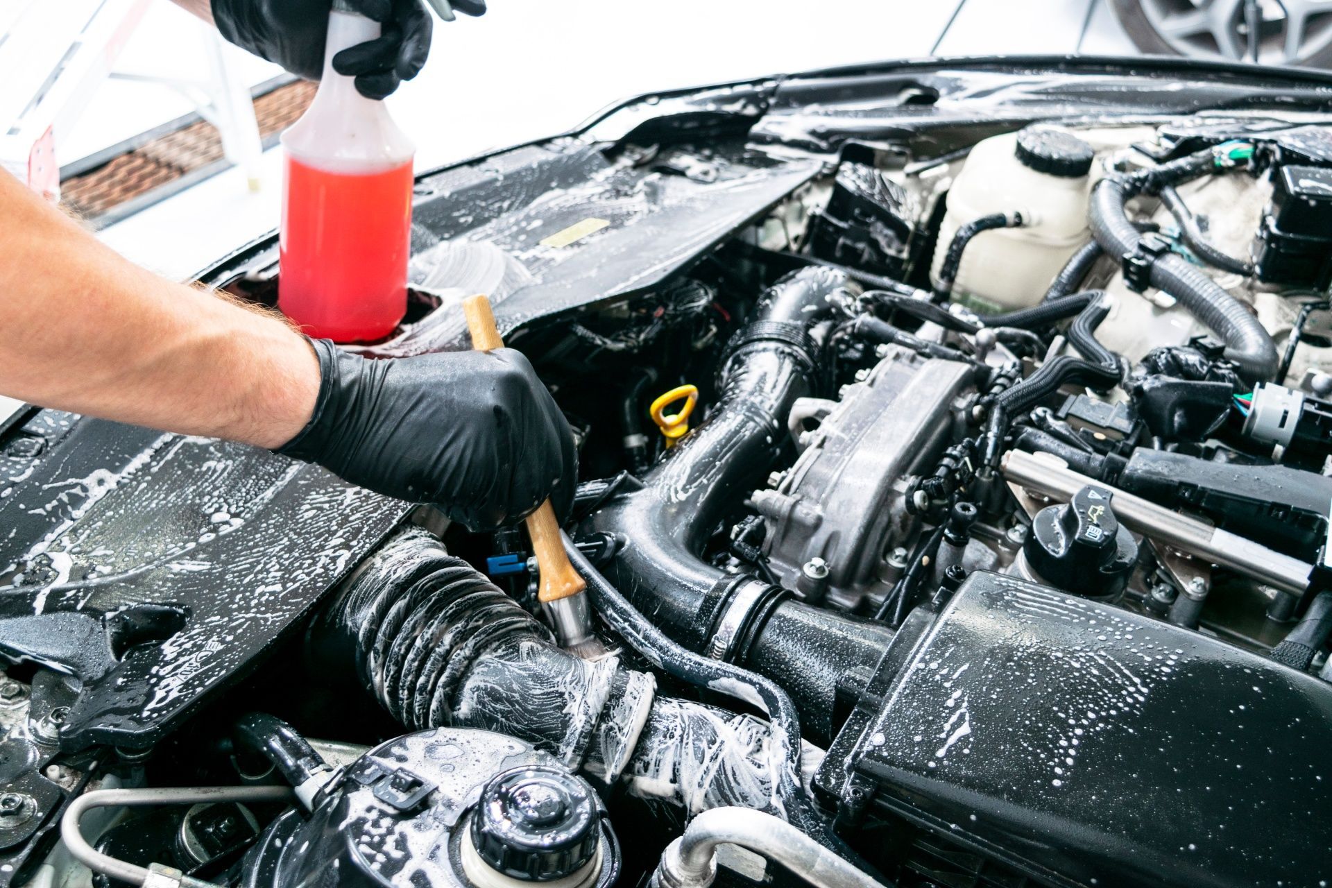 A person is cleaning the engine of a car with a brush.