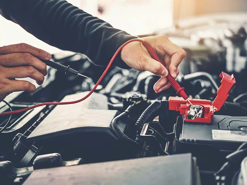 A man is working on a car battery with a multimeter.