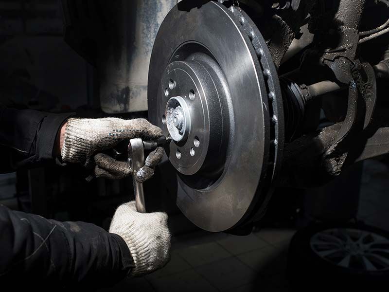 A man is fixing a brake disc on a car with a wrench.