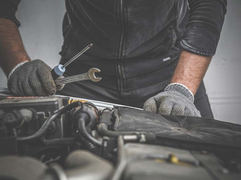 A man is working on a car engine with a wrench.