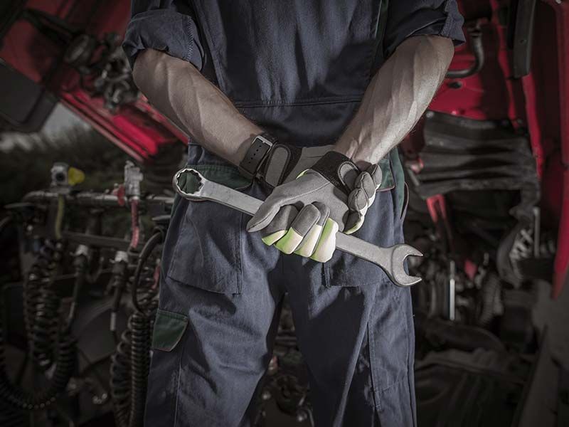 A mechanic is holding a wrench behind his back in a garage.