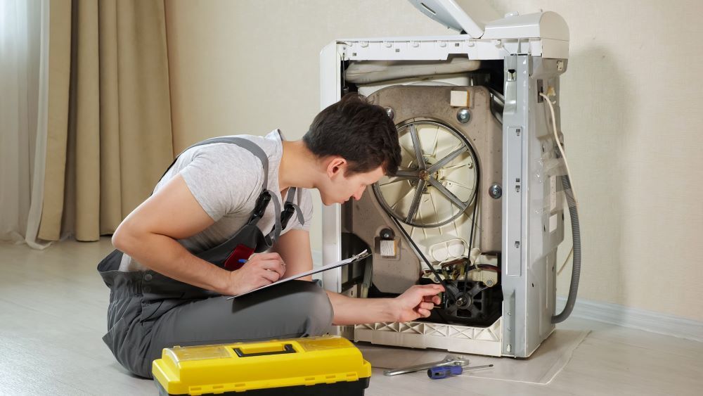 A Man Is Sitting on The Floor Fixing a Washing Machine — Fast Tech Appliance Repairs in Lake Macquarie, NSW