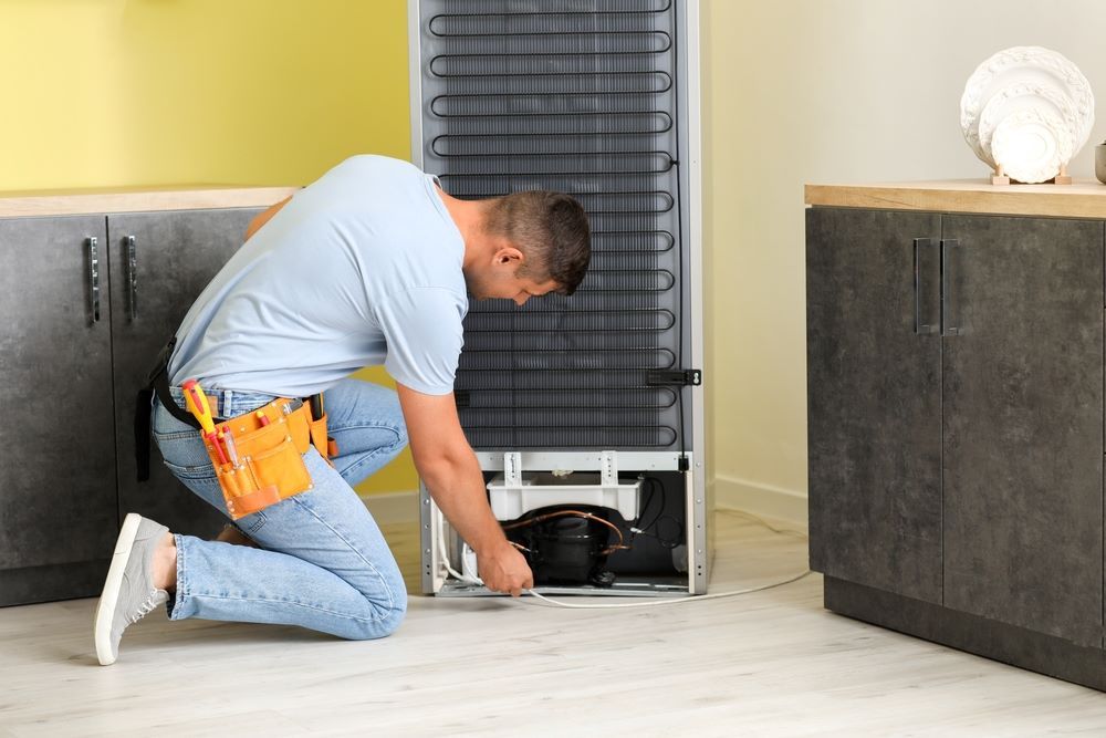 A Man is Repairing a Refrigerator in a Kitchen — Fast Tech Appliance Repairs in Lake Macquarie, NSW