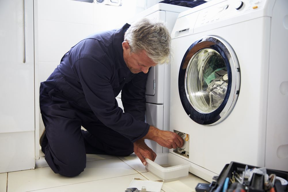 A Man Is Fixing a Washing Machine in A Laundry Room — Fast Tech Appliance Repairs in Newcastle, NSW