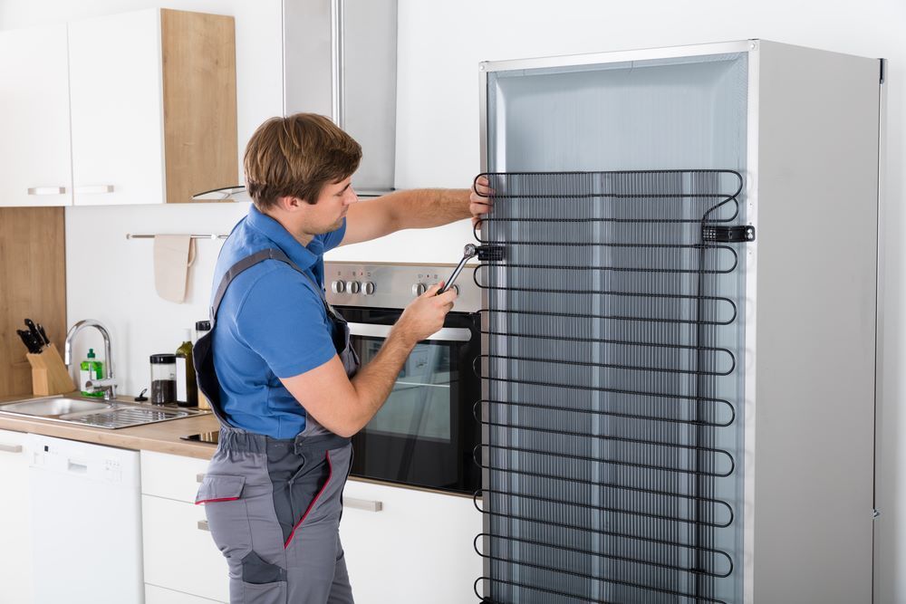A Man Is Fixing a Refrigerator in A Kitchen — Fast Tech Appliance Repairs in Lake Macquarie, NSW
