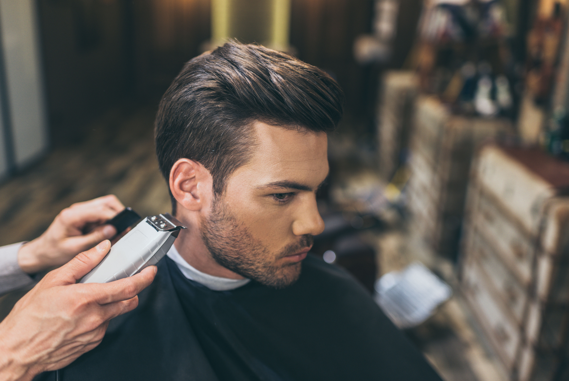 Man getting a haircut at a salon; barber uses clippers on side of head.