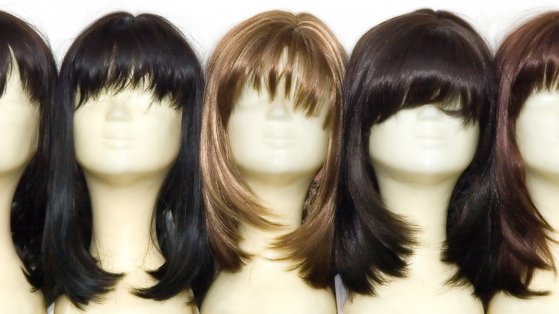 Five wigs on mannequin heads in various colors.
