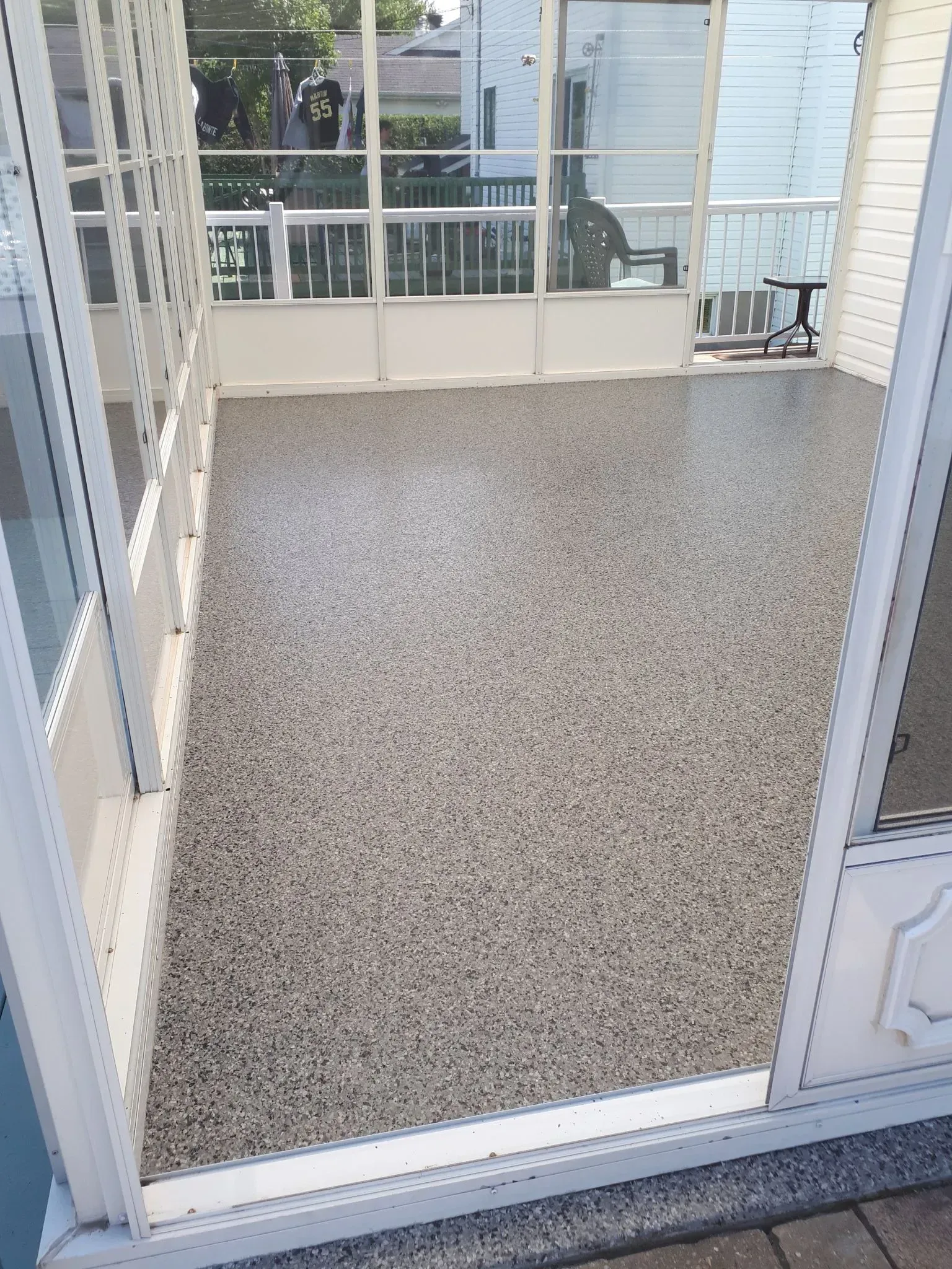 A screened-in porch with a speckled, multi-toned gray epoxy floor, looking out onto a residential yard.