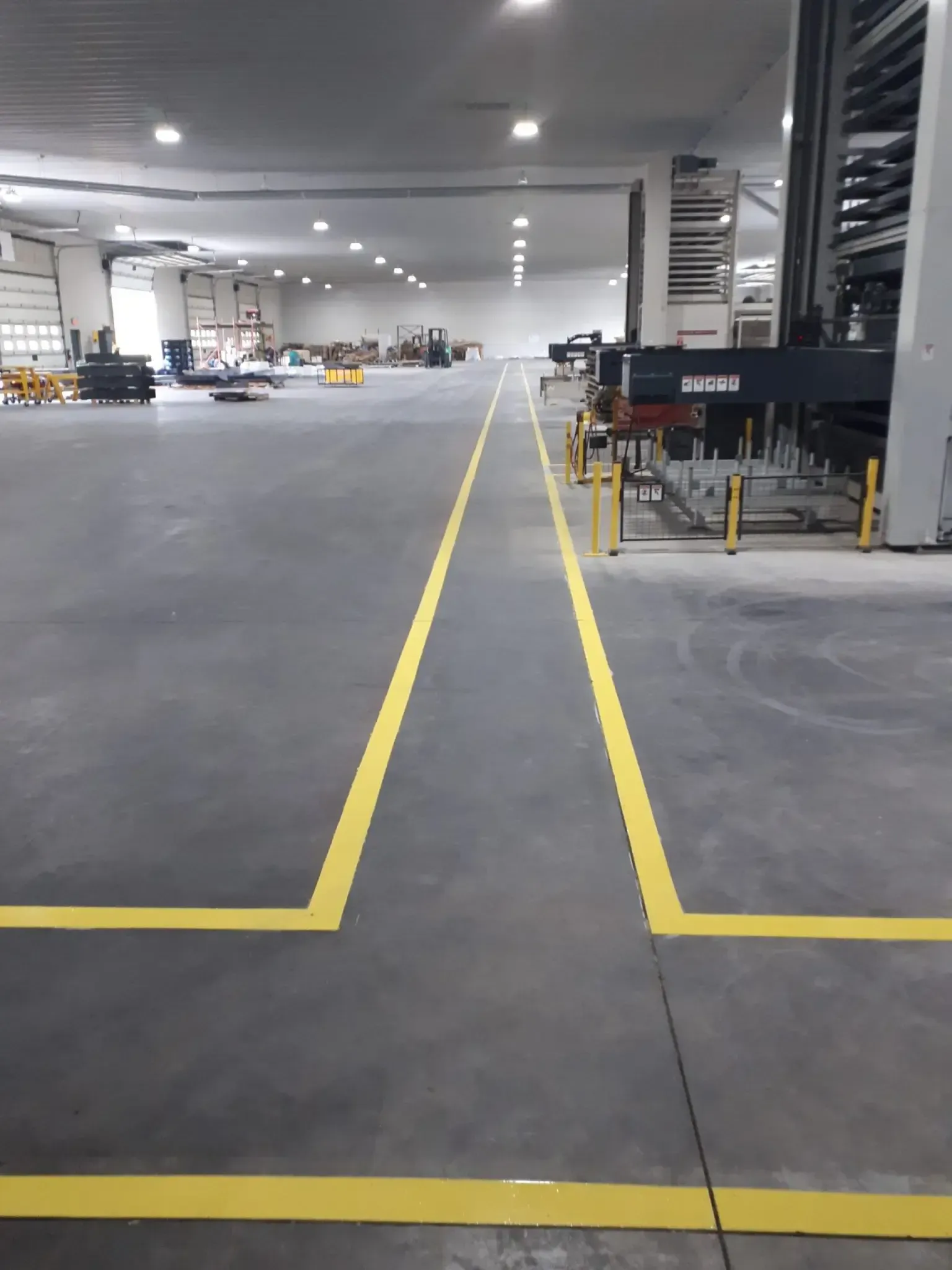 Yellow lines mark a path in a large industrial warehouse with equipment and lighting.