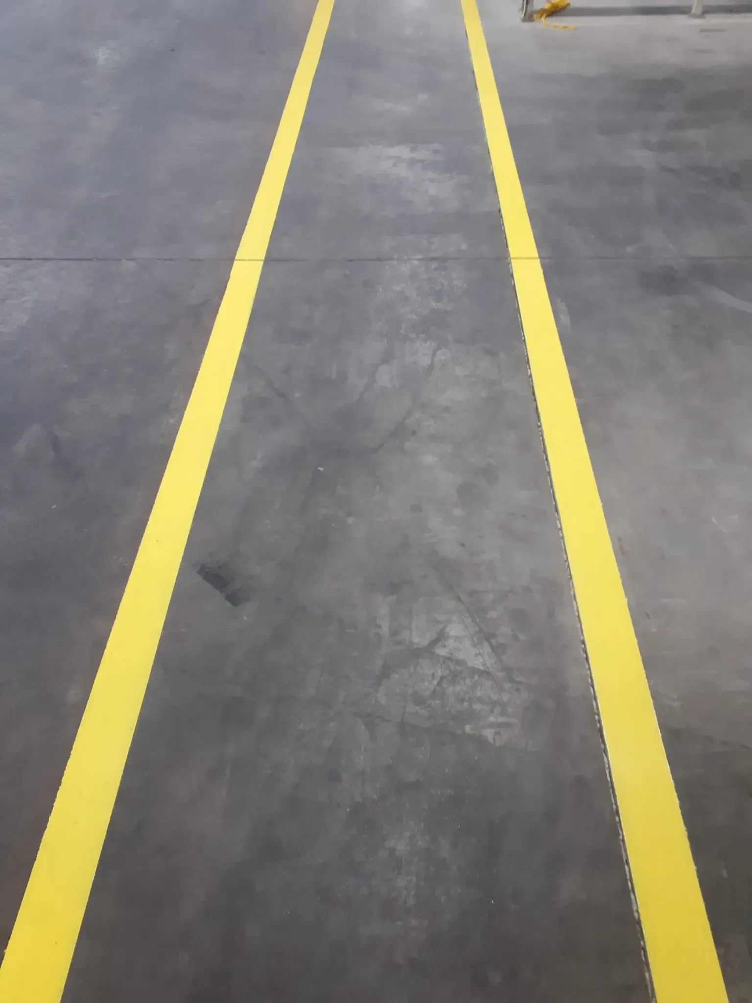 Two parallel yellow lines painted on a gray concrete floor, defining a pathway.