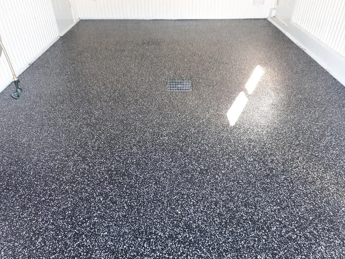 A smooth, glossy garage floor with a black and white speckled epoxy finish and a central floor drain.