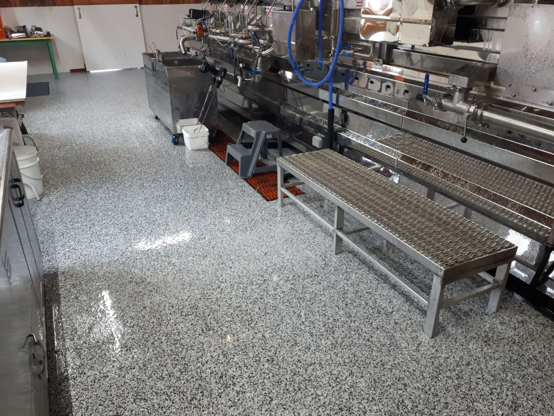 A commercial kitchen area featuring a reflective, speckled epoxy floor with stainless steel machinery and benches.