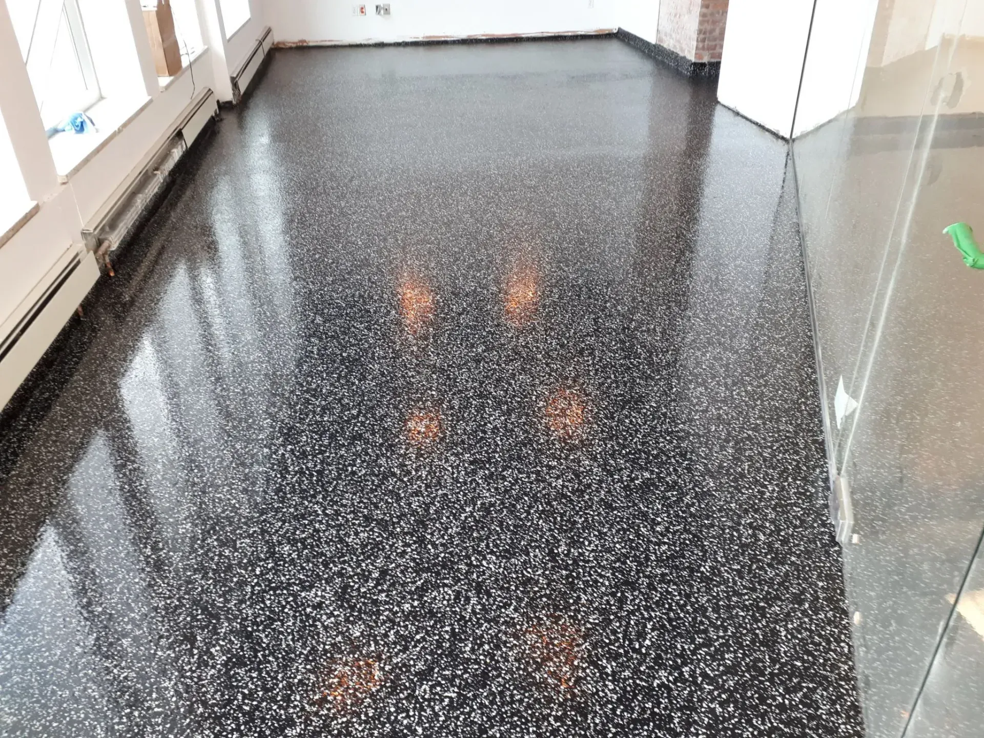 A high-angle view of a polished dark gray terrazzo floor with white flecks, reflecting overhead lights in a modern room.