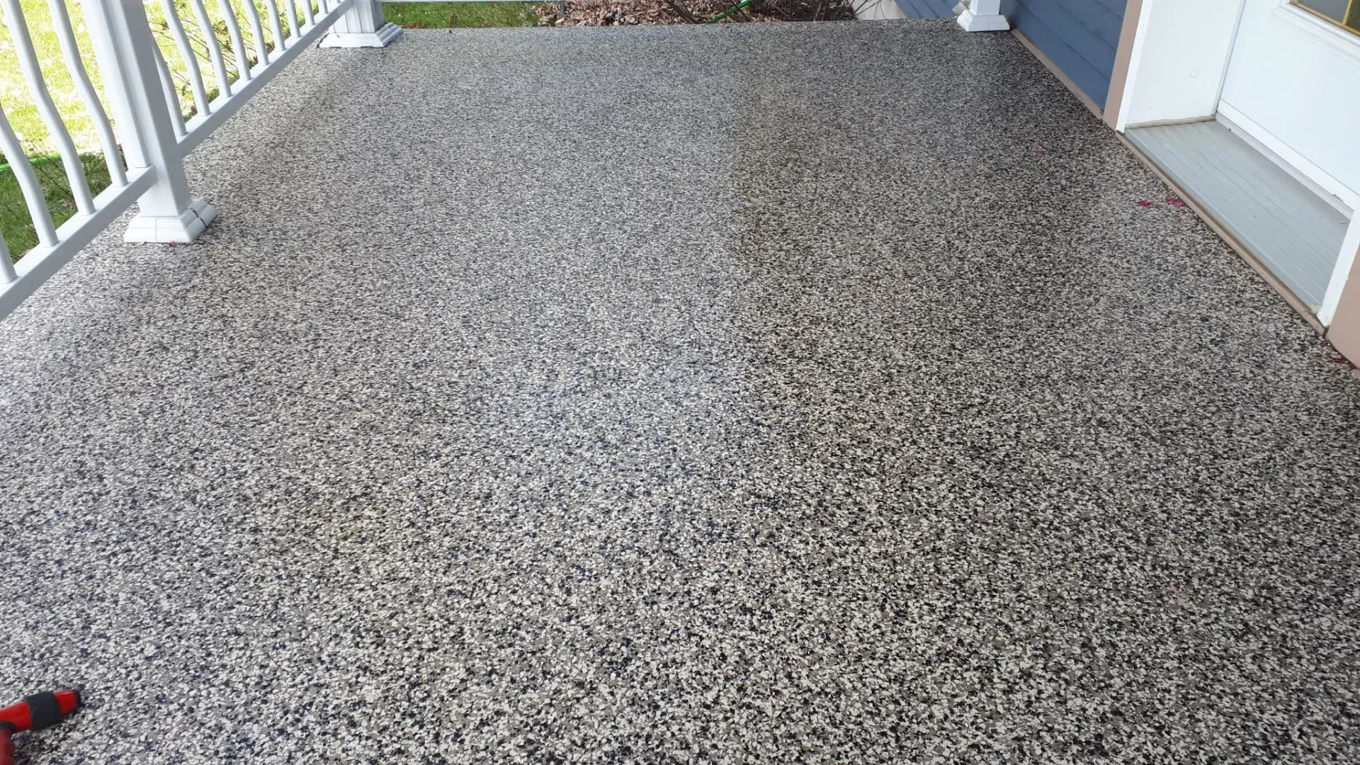 A porch floor featuring a decorative, multi-colored speckled epoxy coating in shades of black, gray, and white.