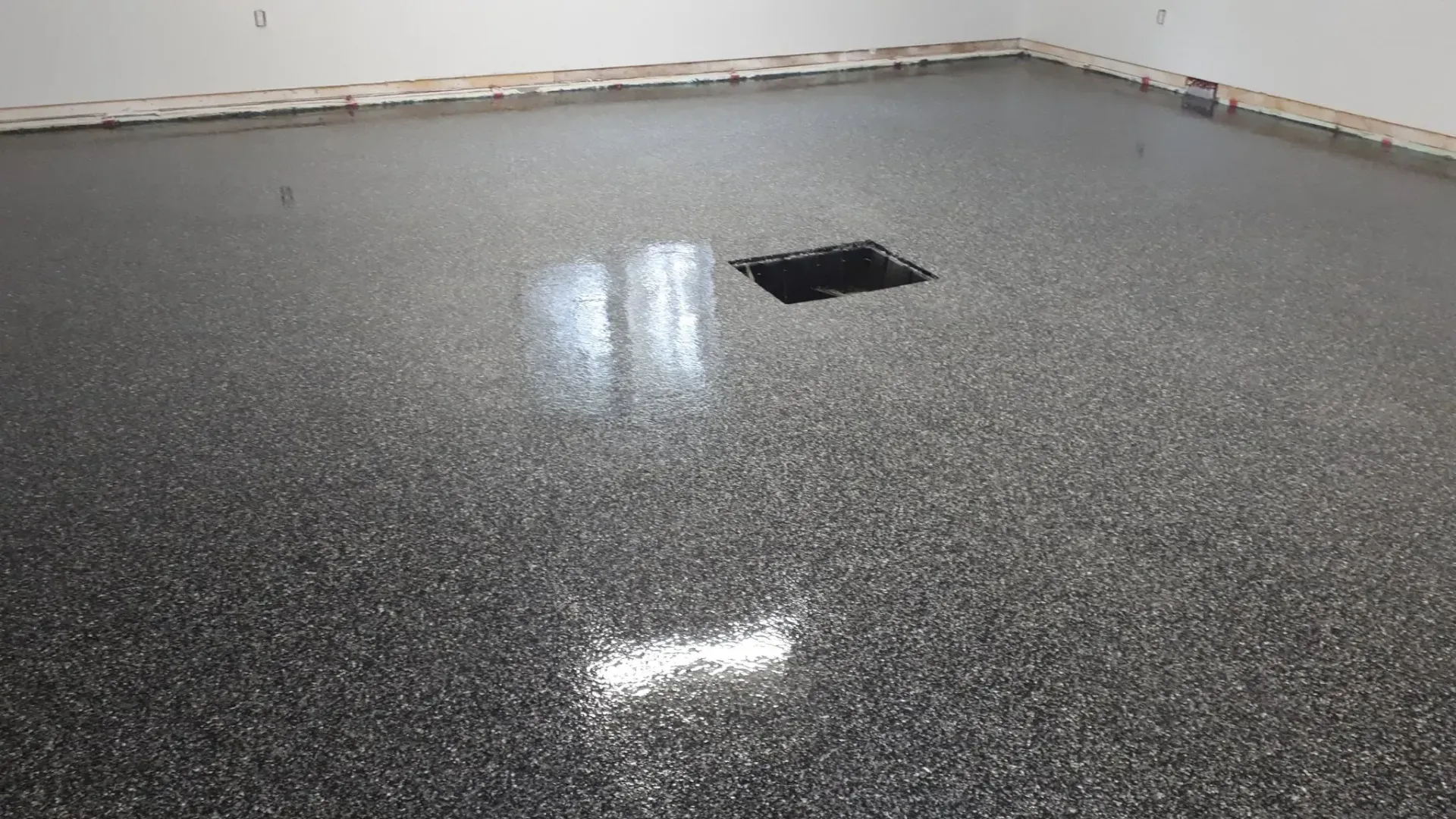 A newly installed gray and black speckled epoxy floor with a high-gloss finish in a room with white walls and a drain.