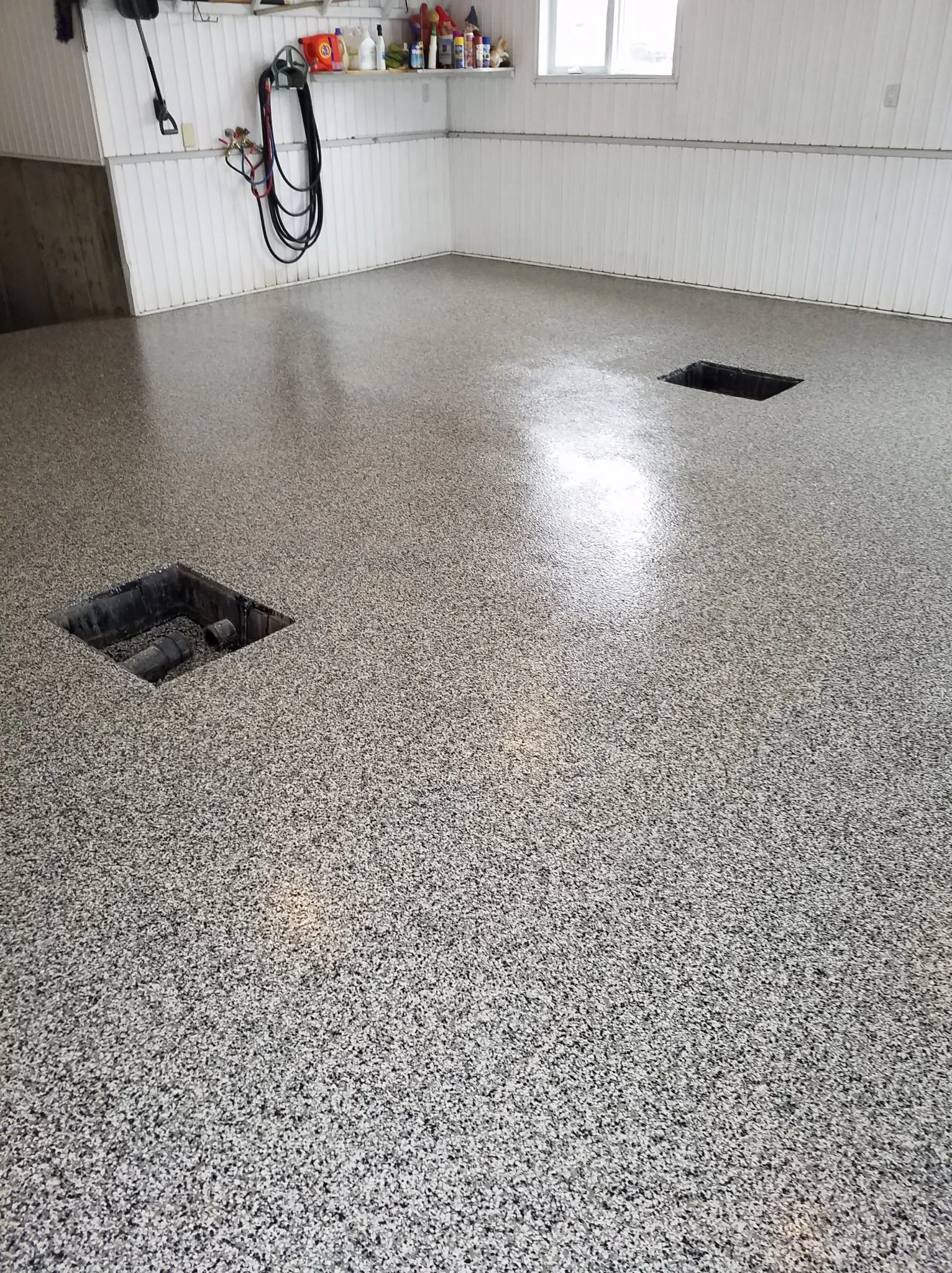 A shiny, speckled gray and black epoxy garage floor with two open utility access panels.
