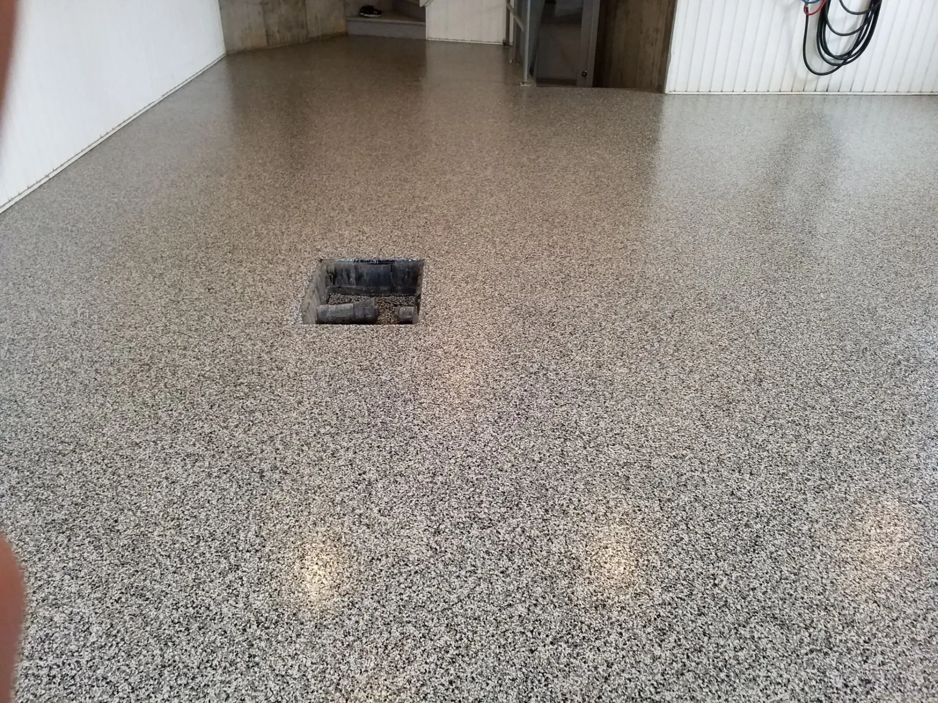 A glossy garage floor covered in a black, white, and grey speckled epoxy flake finish, with a central floor drain.