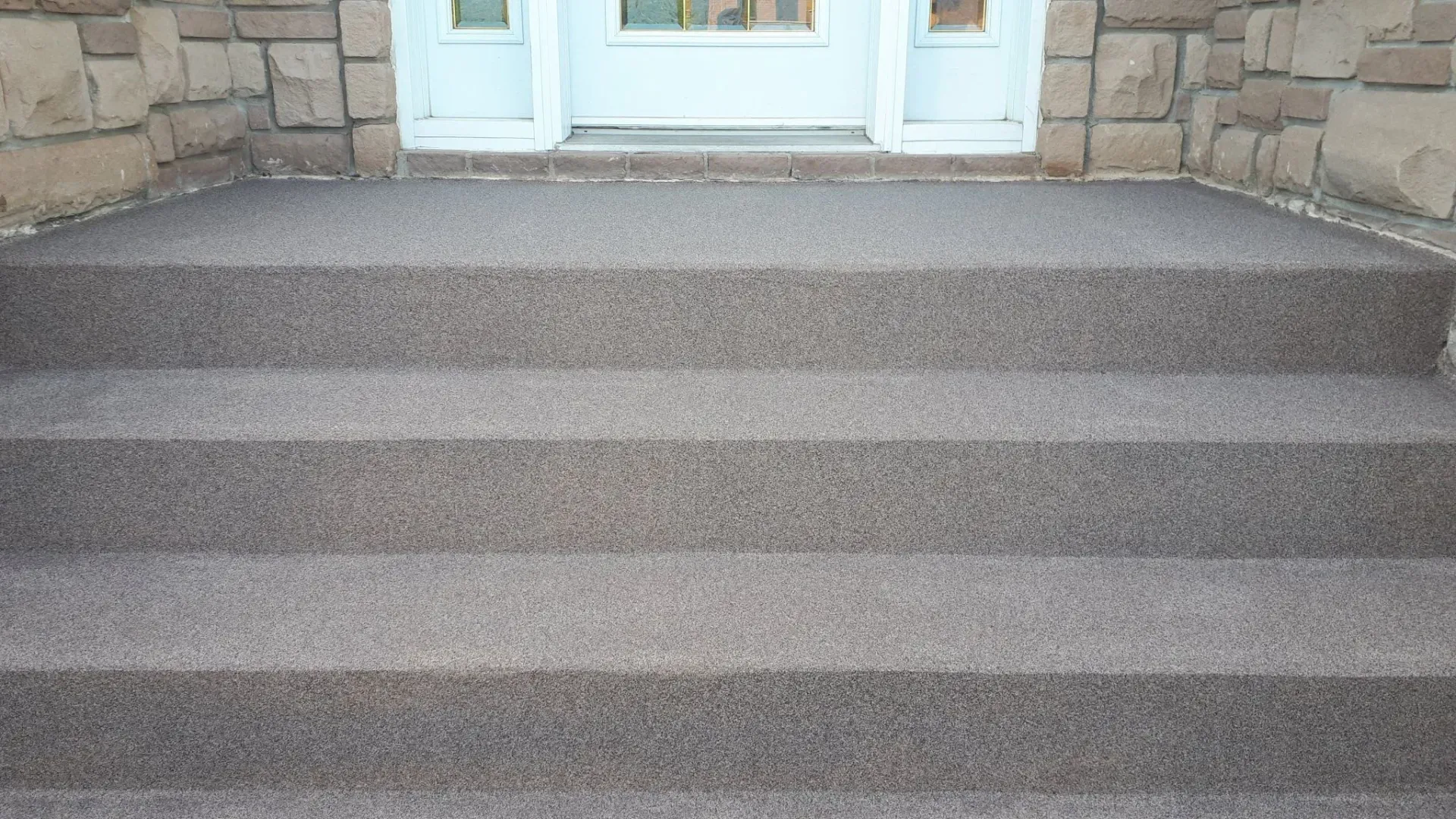 Three steps leading up to a white door. The steps and landing are covered in textured gray aggregate.