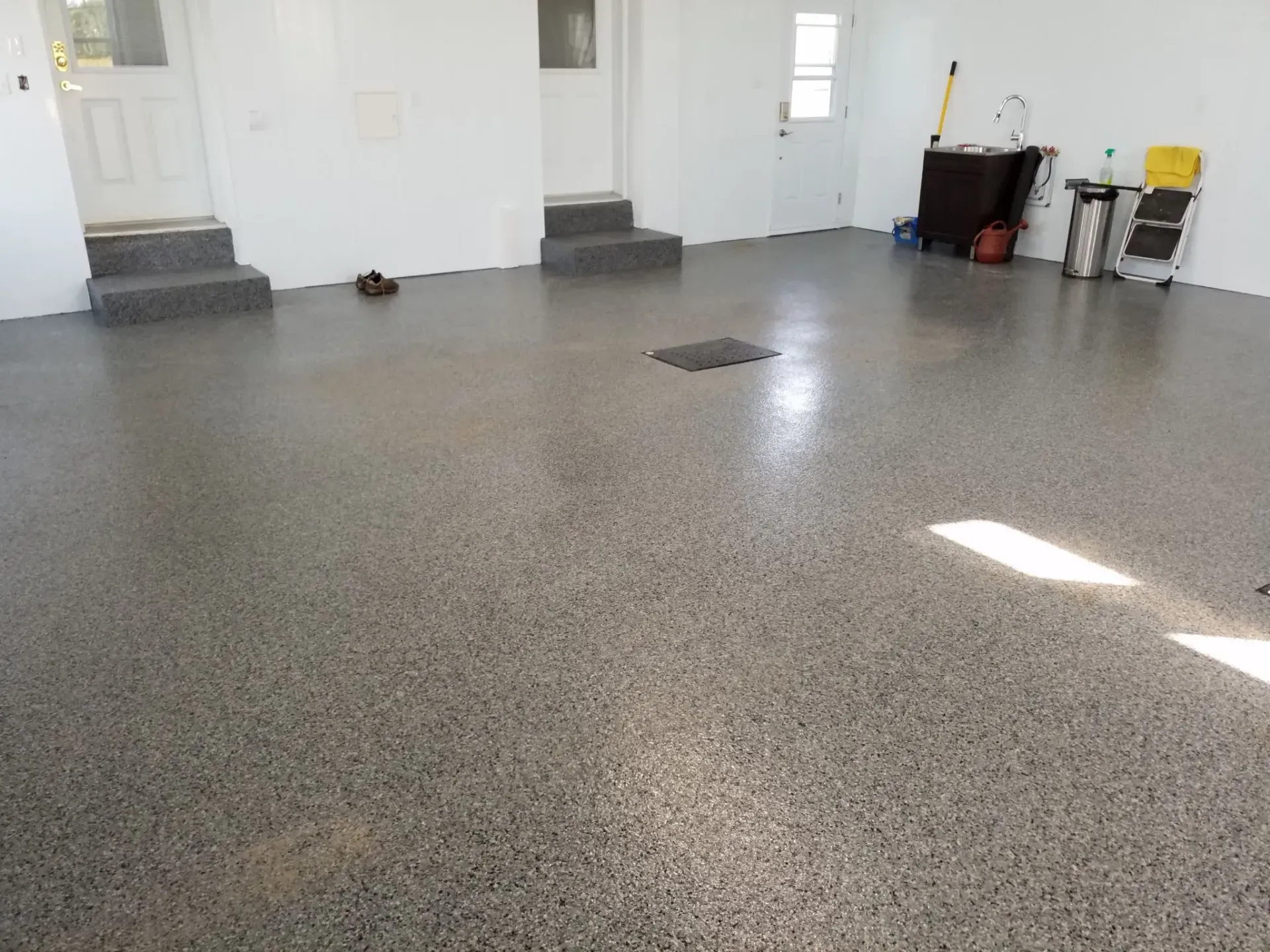 A spacious garage with a grey, speckled epoxy floor, white walls, and three entry doors.
