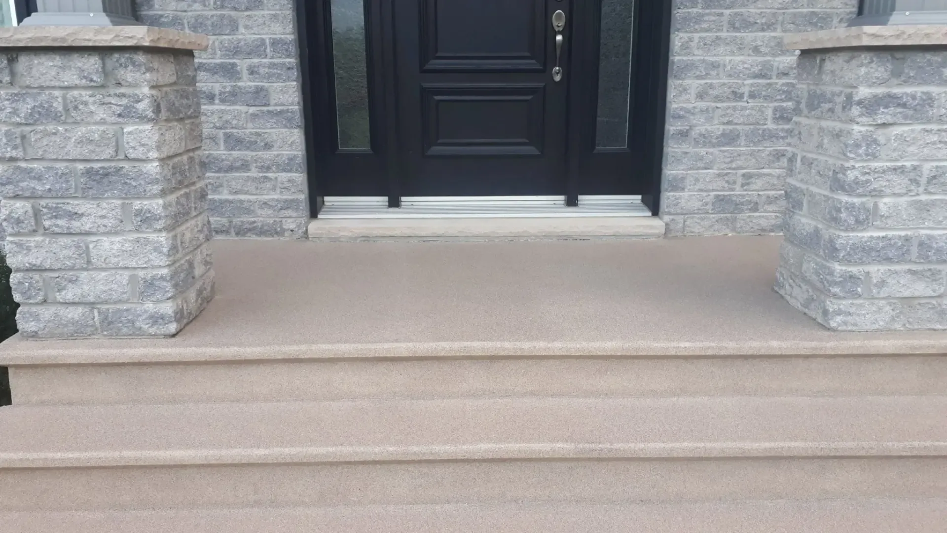 Exterior entrance with stone columns, dark door, and textured steps.