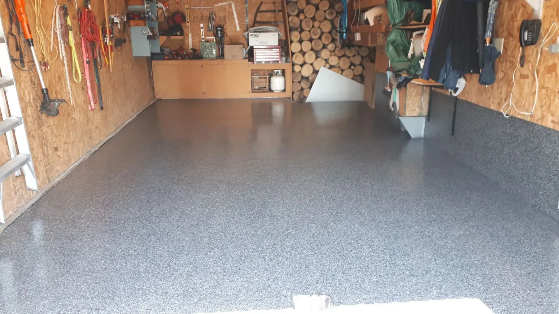 Garage interior with a gray speckled epoxy floor, tools on the walls, and a wood storage area.