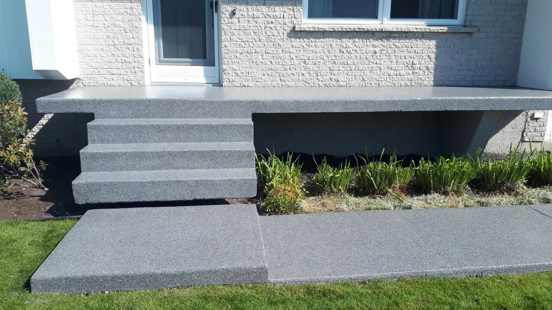 Gray concrete steps leading to a house entrance with gray stone brick facade.