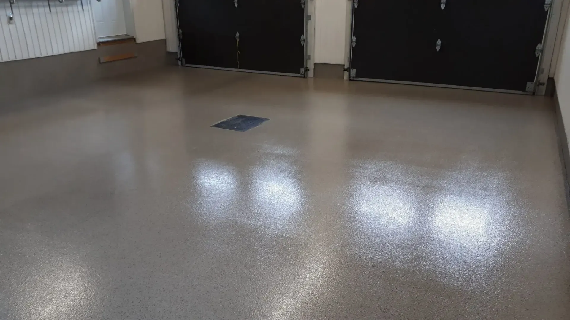 Shiny gray epoxy floor in a garage with black garage doors.