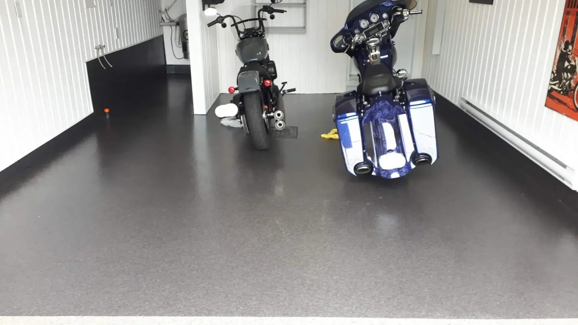 Two motorcycles inside a trailer with a dark gray floor and white walls.